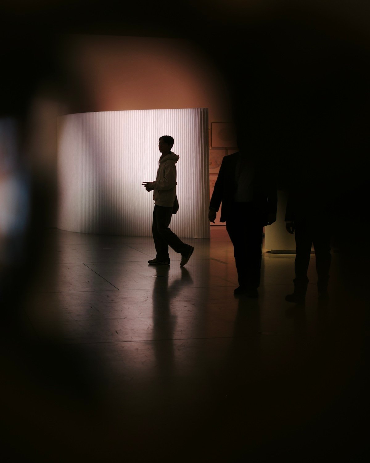 ظلال زوار يتنقلون داخل صالة معرض خافتة الإضاءة