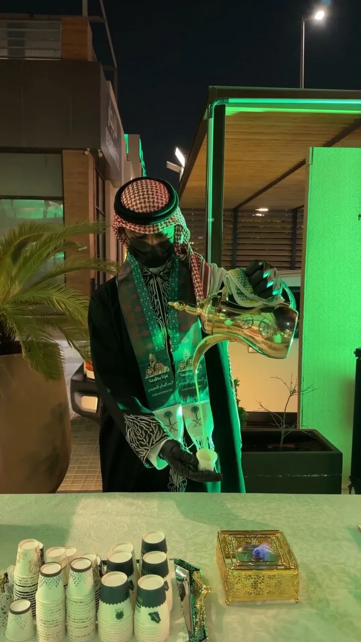 قهوجي بالزي التراثي يصب القهوة من الدلة أمام المحل