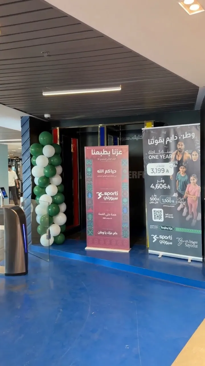 أعمدة بالونات خضراء وبيضاء ولافتات المناسبة عند مدخل الصالة
